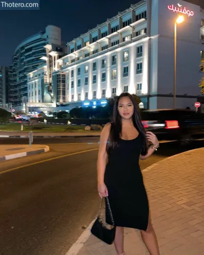 Camii_tg - woman in a black dress standing on a sidewalk in front of a building