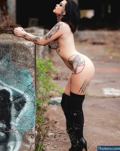 EvilZatanna - a woman with tattoos on her body leaning against a wall