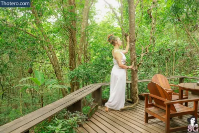 Peregrina - woman in white dress standing on a deck in the woods