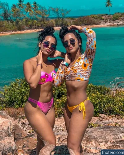 Mariely E Mirella Santos - two women in bikinis posing for a picture on a rocky beach