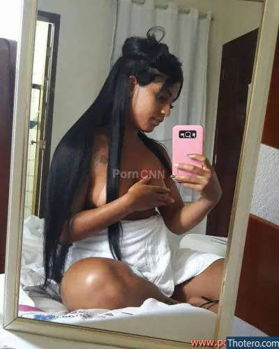 Mulher Mamao - woman with long black hair sitting on a bed looking at her cell phone