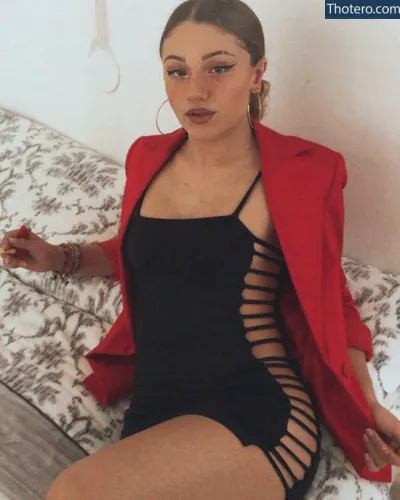 janiiss - woman in a black dress and red jacket sitting on a bed