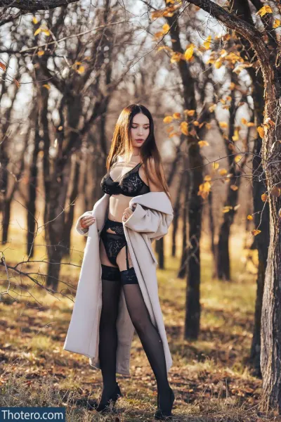 April Alba - a woman in a white coat and black stockings posing in a forest