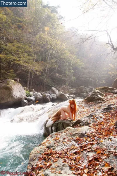 Saku Cosplay - there is a woman sitting on a rock next to a river