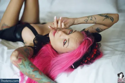 iamdollhead - woman with pink hair laying on a bed with a tattoo on her arm