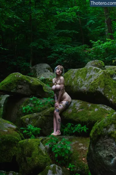 Elles - woman sitting on a rock in the woods with a tattoo on her arm