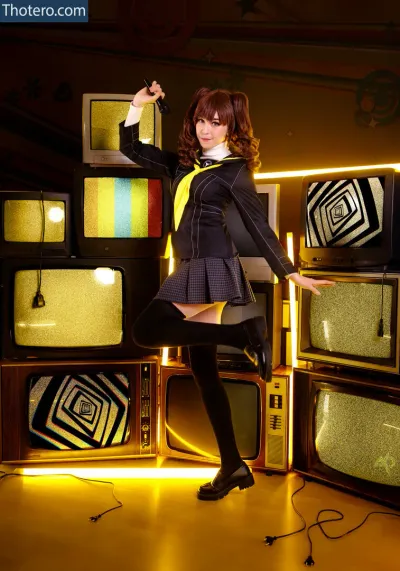 Inochi - woman in a black dress and yellow vest posing in front of a stack of televisions