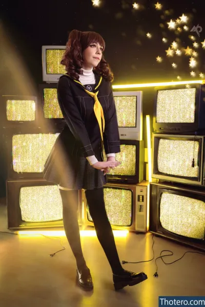 Inochi - woman in a black dress and yellow tie standing in front of a wall of televisions