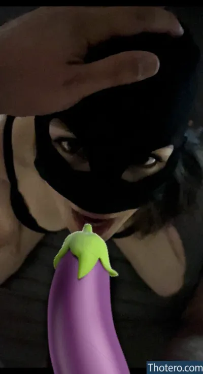 LucieAzarro - woman in a mask holding a purple eggplant