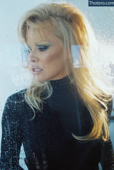 Pamela Anderson - blond woman in wetsuit looking out of window with rain on her face