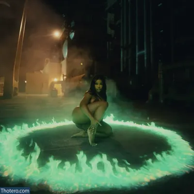 SZA - a woman kneeling on the ground in front of a fire circle