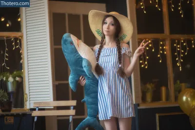 Alina Latypova - dressed in a striped dress and straw hat holding a stuffed shark