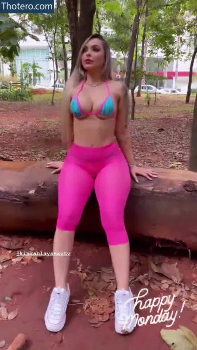 Kiara B - a woman in pink pants and a bikini top sitting on a log