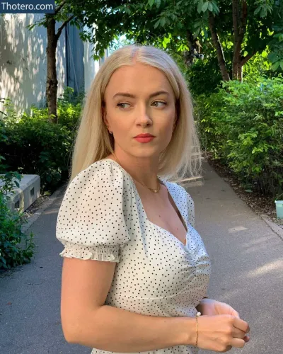Mimi Lintrup - blond woman in a white dress standing on a sidewalk in a park