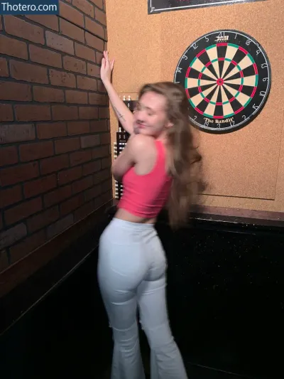 Try Channel Girls - woman in white pants and pink top standing in front of a dart board