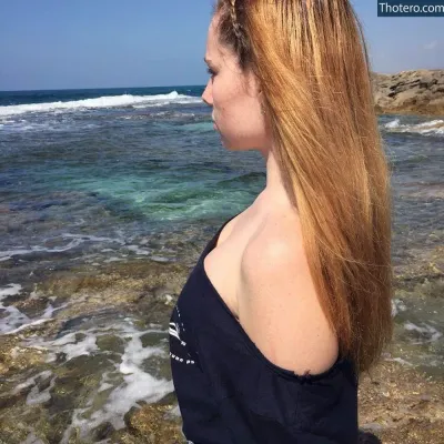 Katya Fisher - woman with long red hair standing on a rocky beach