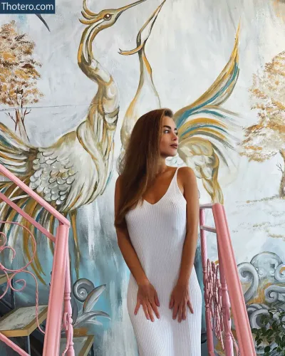 Sasha Shenderey - woman in a white dress standing on a pink staircase