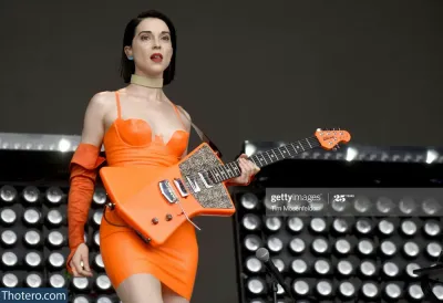St Vincent - a woman in an orange dress plays a guitar on stage