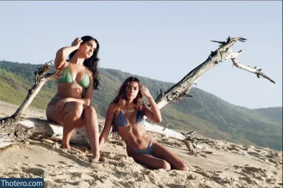 Geraldine Viswanathan - two women in bikinis sitting on a beach next to a tree