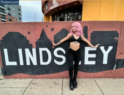 lindseyparanormal - woman with pink hair standing in front of a wall with a sign that says lindsey